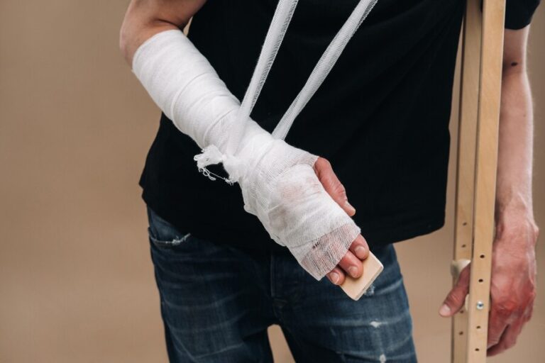 battered-man-with-bandaged-head-cast-his-arm-stands-crutches-gray-background_217593-8173